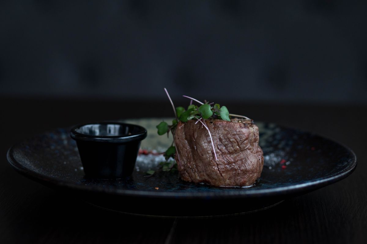 Filet au poivre topped with fresh herbs on a black plate