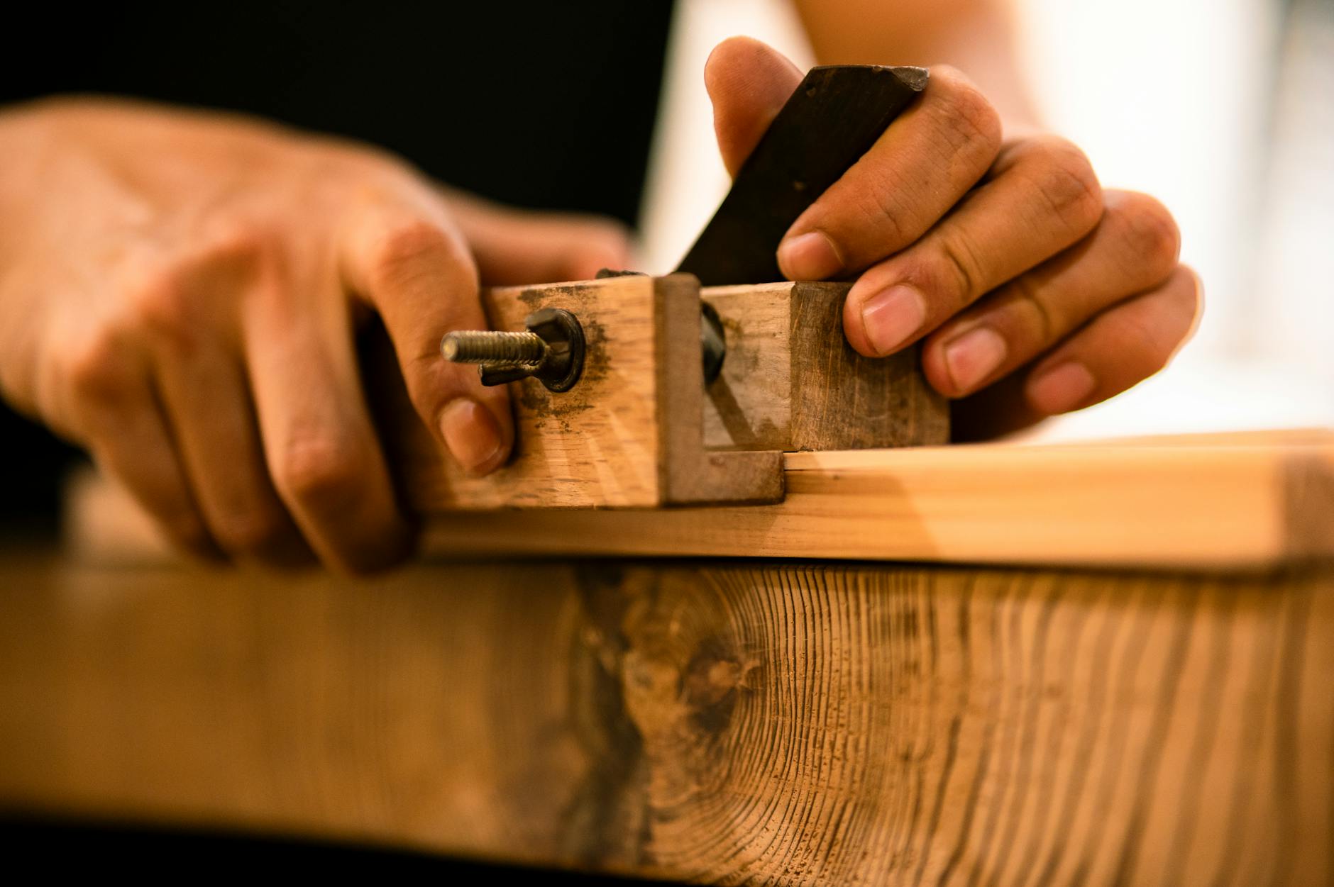 Hands working a wooden plane across a fresh plank